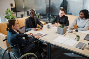 successful businesswoman using wheelchair at meeting and talking to colleagues in office space
