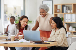 Diverse group of smiling business women using a laptop for discussing online training 