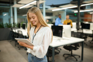 smiling female manager holds tablet device while taking scorm courses online in office