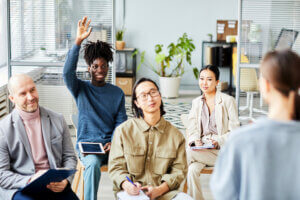 Young male employee raises hand for question during a workplace training courses in office
