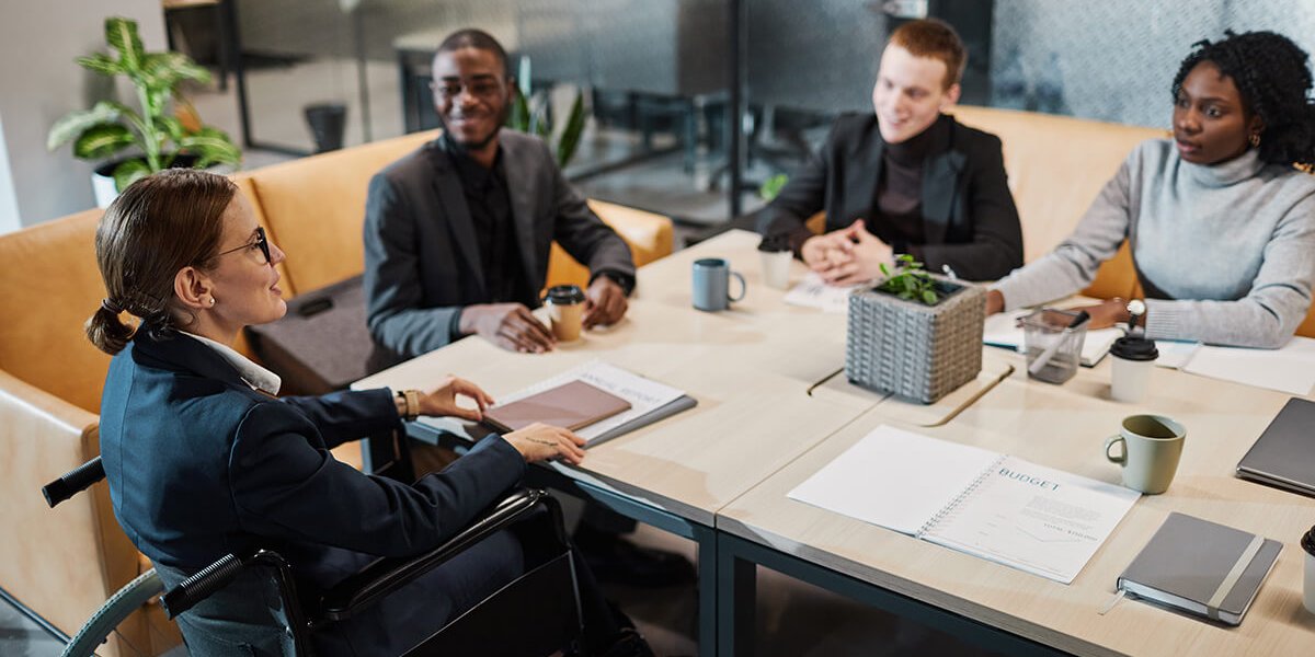 successful businesswoman using wheelchair at meeting and talking to colleagues in office space