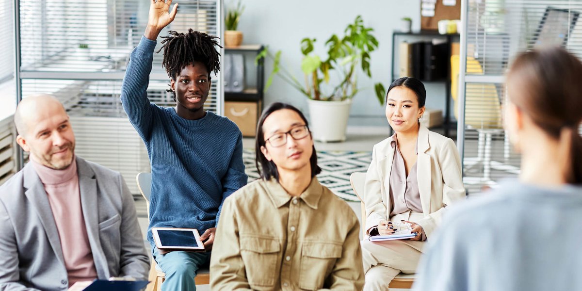 Young male employee raises hand for question during a workplace training course in office