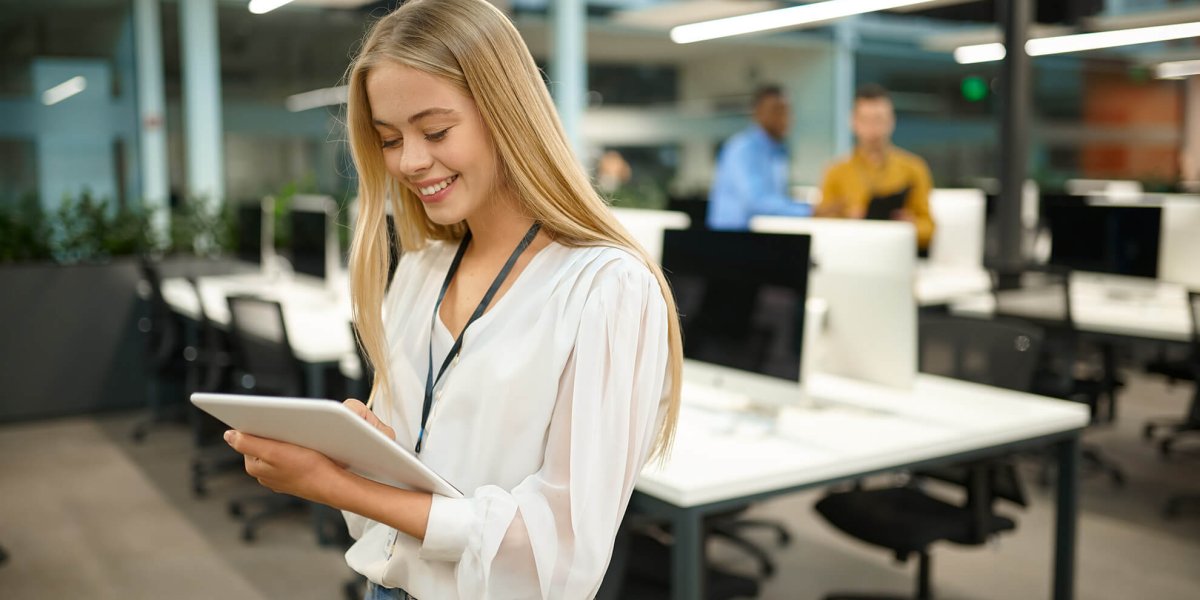 smiling female manager holds tablet device while taking scorm courses online in office